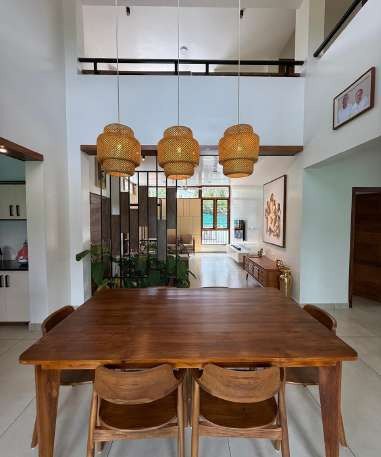 Double-height dining space with a teak table and rattan pendant lights